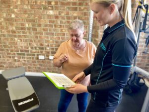 Exercise physiologist standing with middle aged lady with short hair looking at paper for exercise program. 