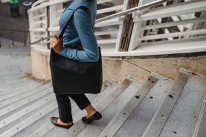 Lady in blue shirt and office work clothes climbing stairs with her black bag over shoulder. 