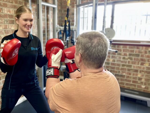 Lady with short hair doing boxing with personal trainer exercise physiologist in gym